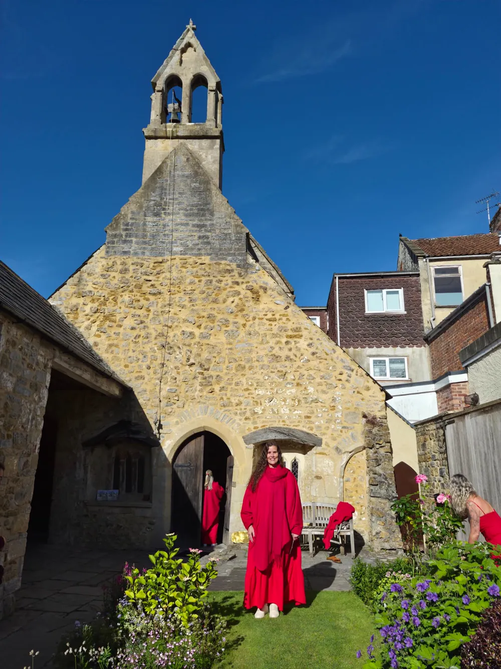 Hérica de vermelho diante de uma capela de pedra em Glastonbury