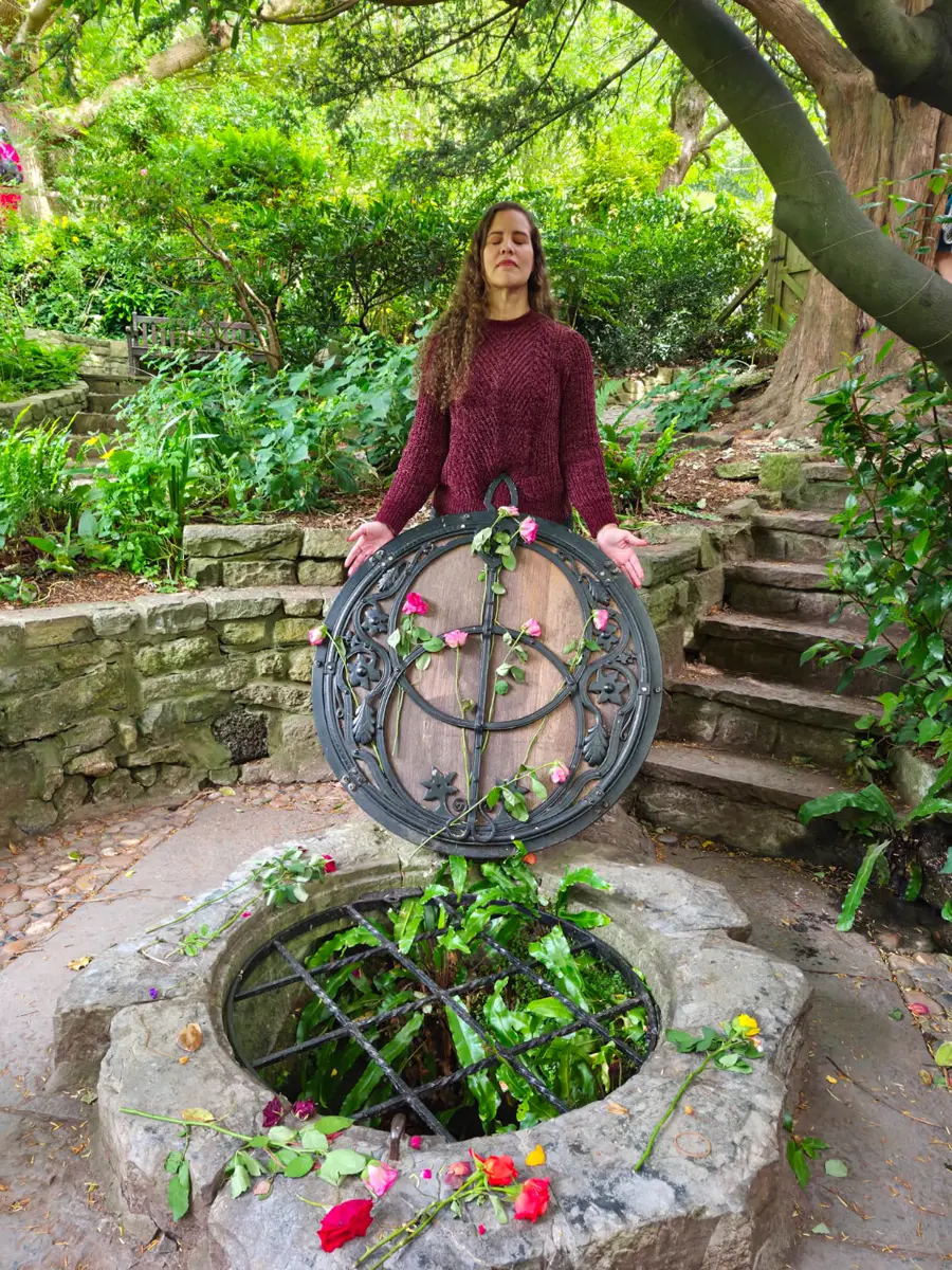 Hérica de olhos fechados diante do poço sagrado, com rosas